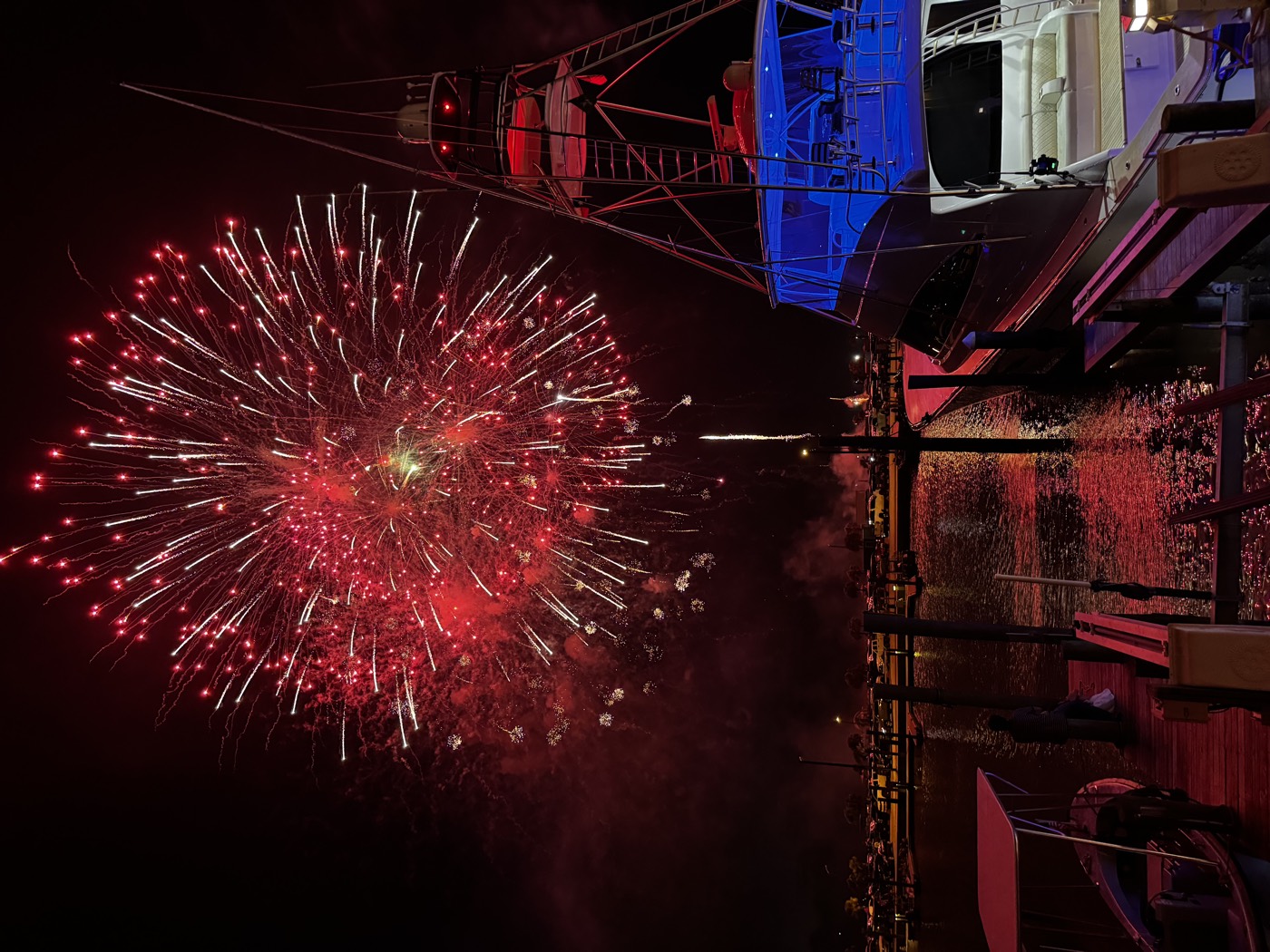 Fourth of July fireworks bursting red over the Port Aransas marina, reflecting on the harbor water beside a docked offshore sportfishing boat lit in blue.